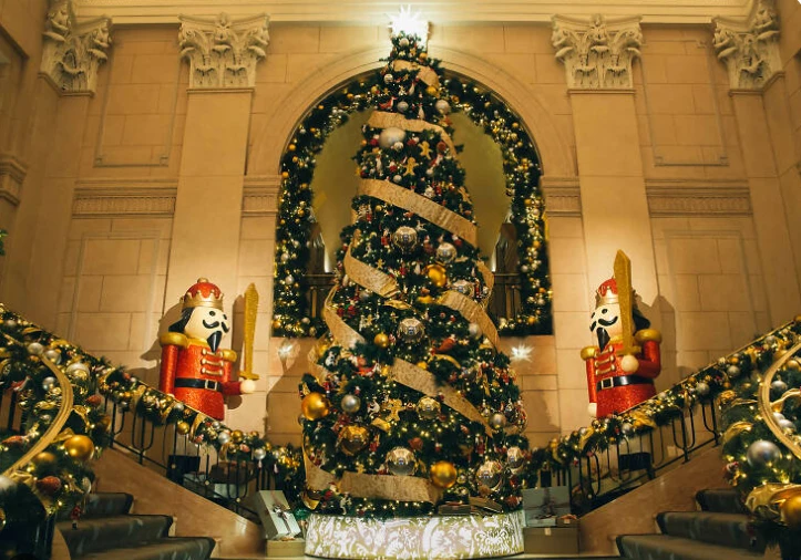 A grand hotel lobby with a towering decorated Christmas tree, nutcrackers, and garland-wrapped staircases